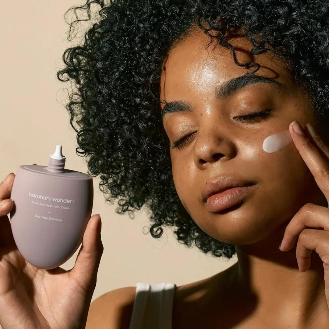 Woman applying HARUHARU Black Rice 10 Hyaluronic Cream 50ml to her face, showcasing skincare routine with product in hand