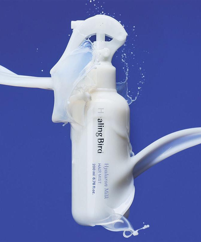HEALING BIRD Hyalutonic Milk Hair Mist 200ml beauty product in white bottle with splashing milk on blue background.