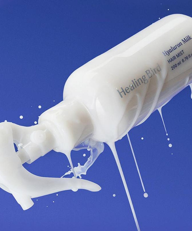 HEALING BIRD Hyalutonic Milk Hair Mist 200ml bottle against blue background, showing milky texture.