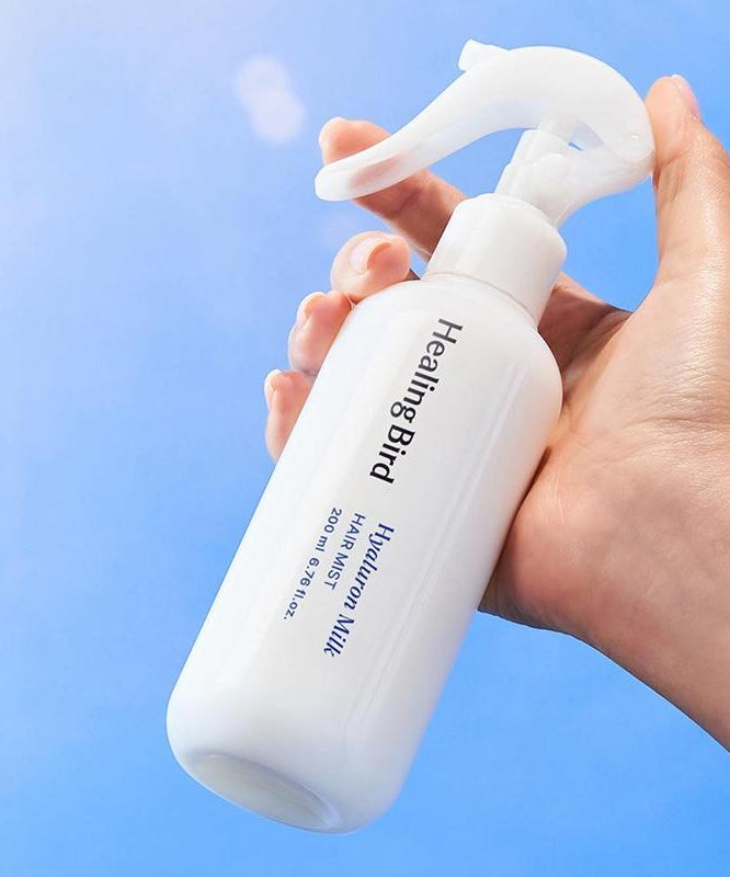 HEALING BIRD Hyalutonic Milk Hair Mist 200ml bottle held in hand against blue background