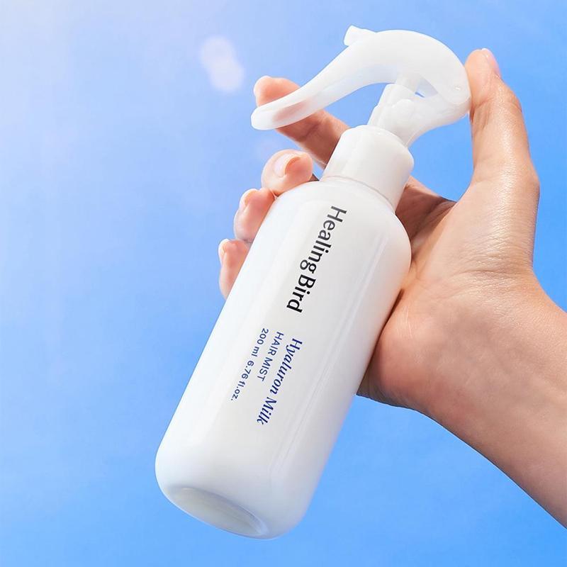 HEALING BIRD Hyalutonic Milk Hair Mist 200ml bottle held in hand against blue background