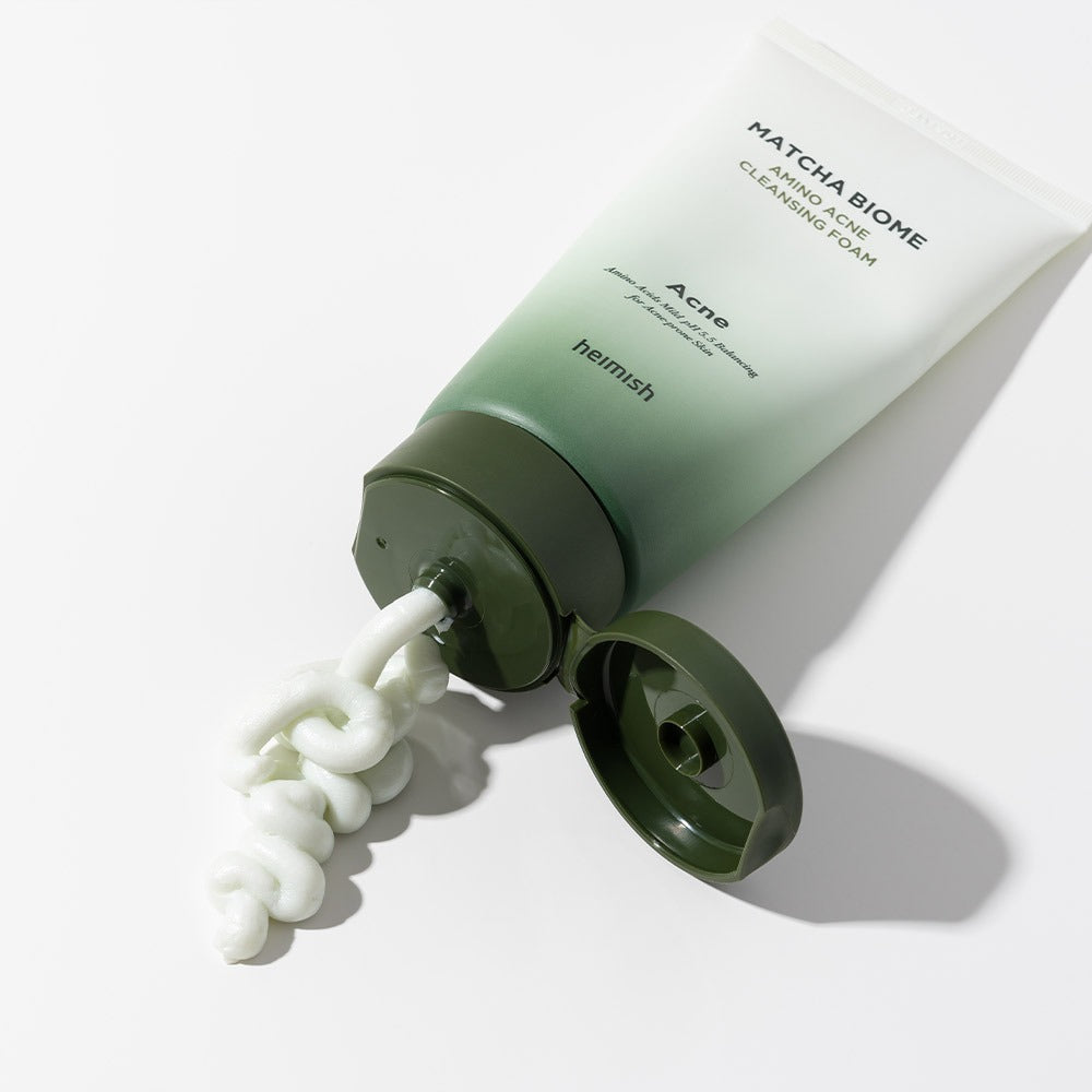 HEIMISH Matcha Biome Amino Acne Cleansing Foam 150g tube with foam oozing out on a white surface, skincare product image.