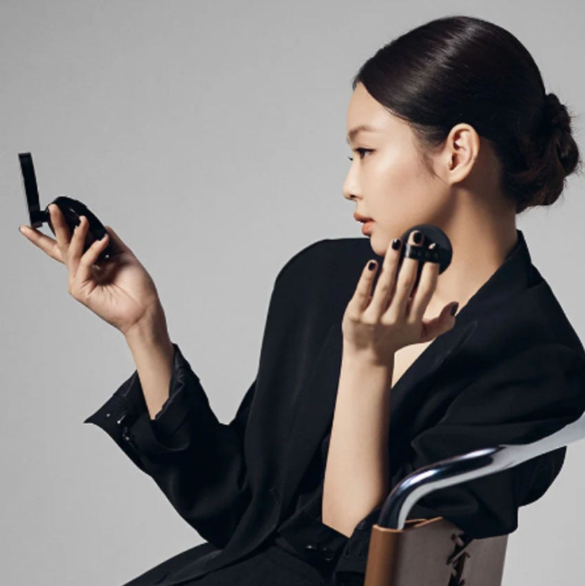 Woman applying HERA Black Cushion Foundation SPF34 PA++ 15g, showcasing sleek compact design and smooth application.