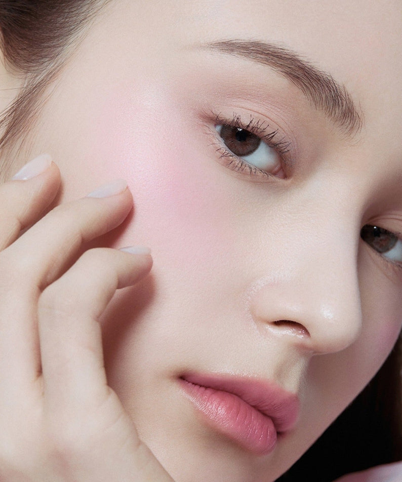 Close-up of a woman applying HERA Hera Blush 5.5g to her cheek for a natural pink glow.