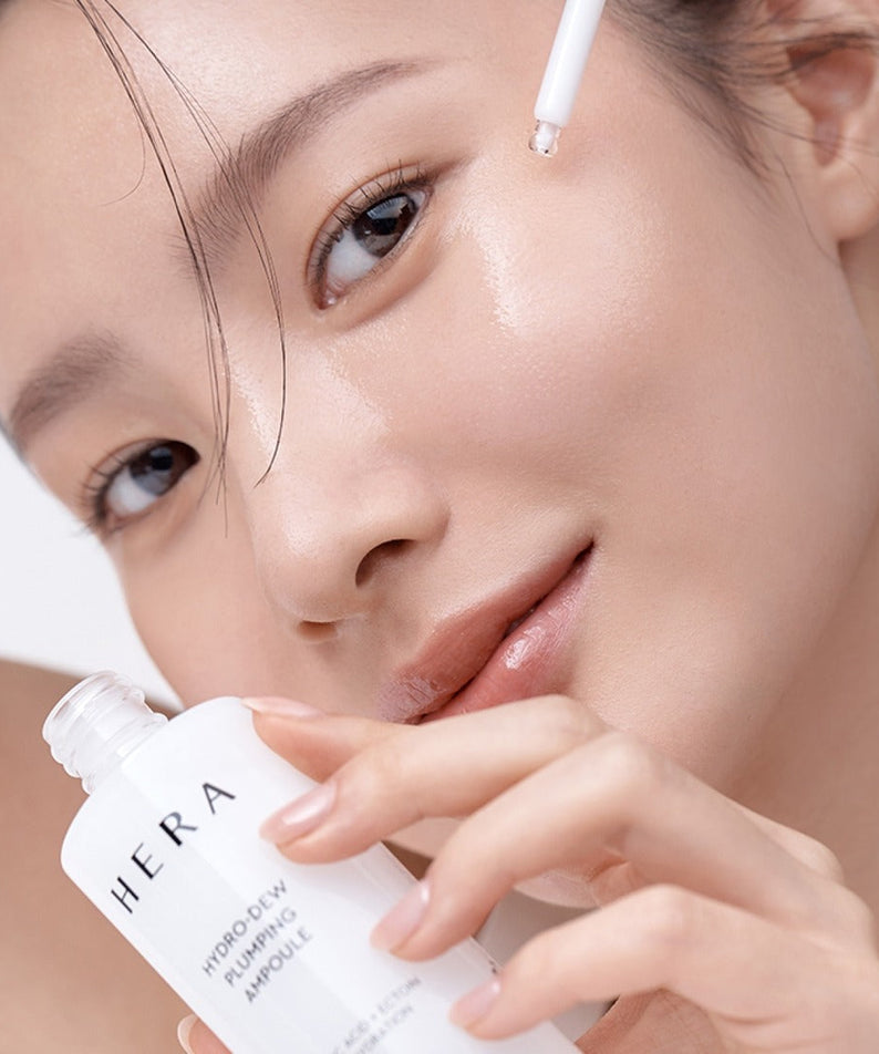 Woman applying HERA Hydro-Dew Plumping Ampoule 50ml on face for hydration and skincare.