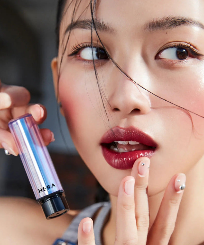 Woman applying HERA Sensual Tinted Shine Stick 3.5g, showcasing vibrant glossy lips and radiant makeup look.