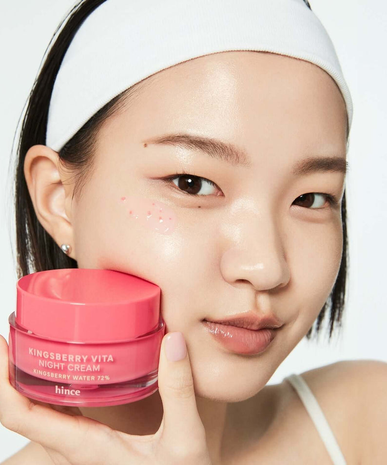 Woman holding HINCE Kingsberry Vita Night Cream jar near her face with a gentle smile.