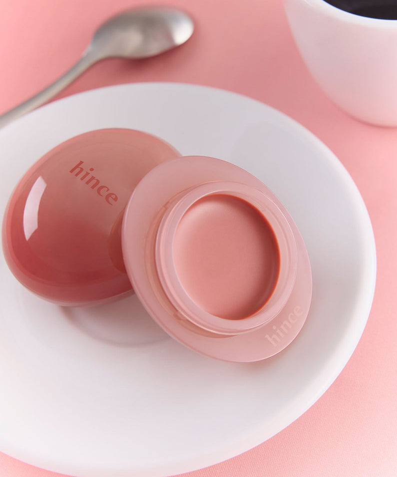 HINCE Low Glow Dewy Ball (Lip&Cheek) on a plate with a spoon and coffee mug, perfect for achieving a dewy lip and cheek look.