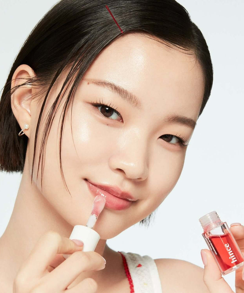 Woman applying HINCE Vita Barrier Nourishing Lip Oil from a small bottle, showcasing glossy lip care product for hydration and nourishment.