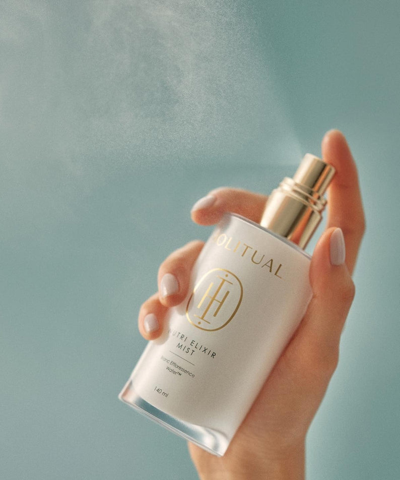 Hand holding a bottle of HOLITUAL Elixir Mist 140ml against a blue background