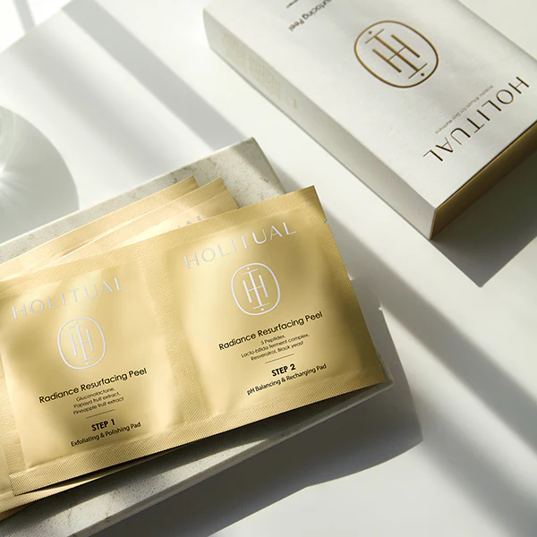 HOLITUAL Radiance Resurfacing Peel packaging on marble tray under sunlight, highlighting the skincare product's exfoliating benefits.