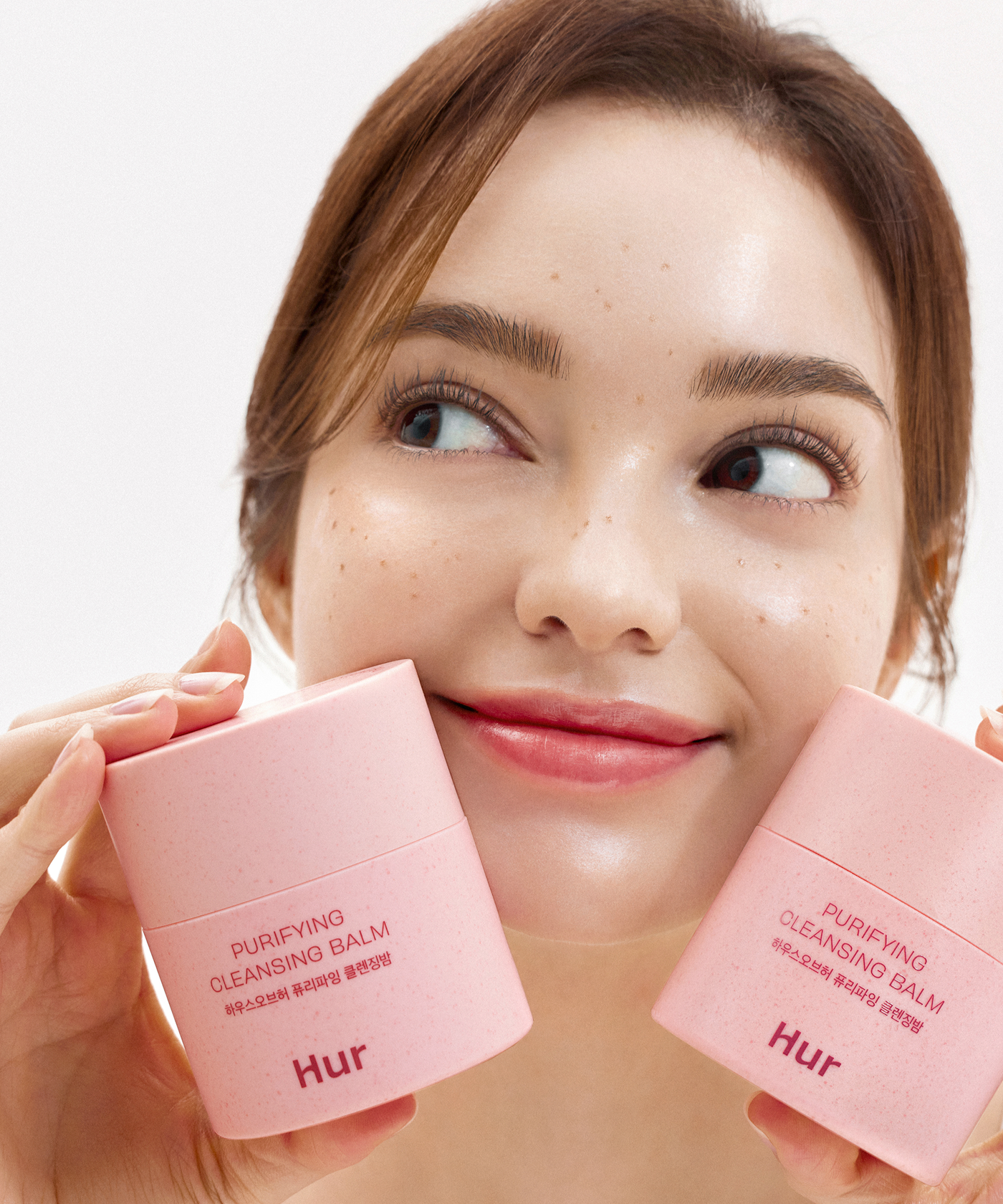 Woman holding HOUSE OF HUR Purifying Cleansing Balm containers, showcasing skincare product