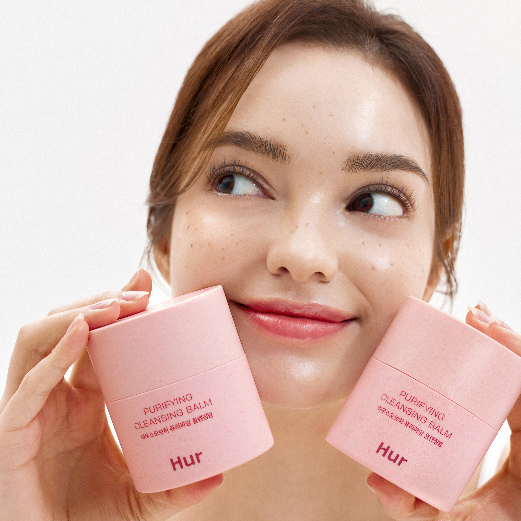 Woman holding HOUSE OF HUR Purifying Cleansing Balm containers, showcasing skincare product