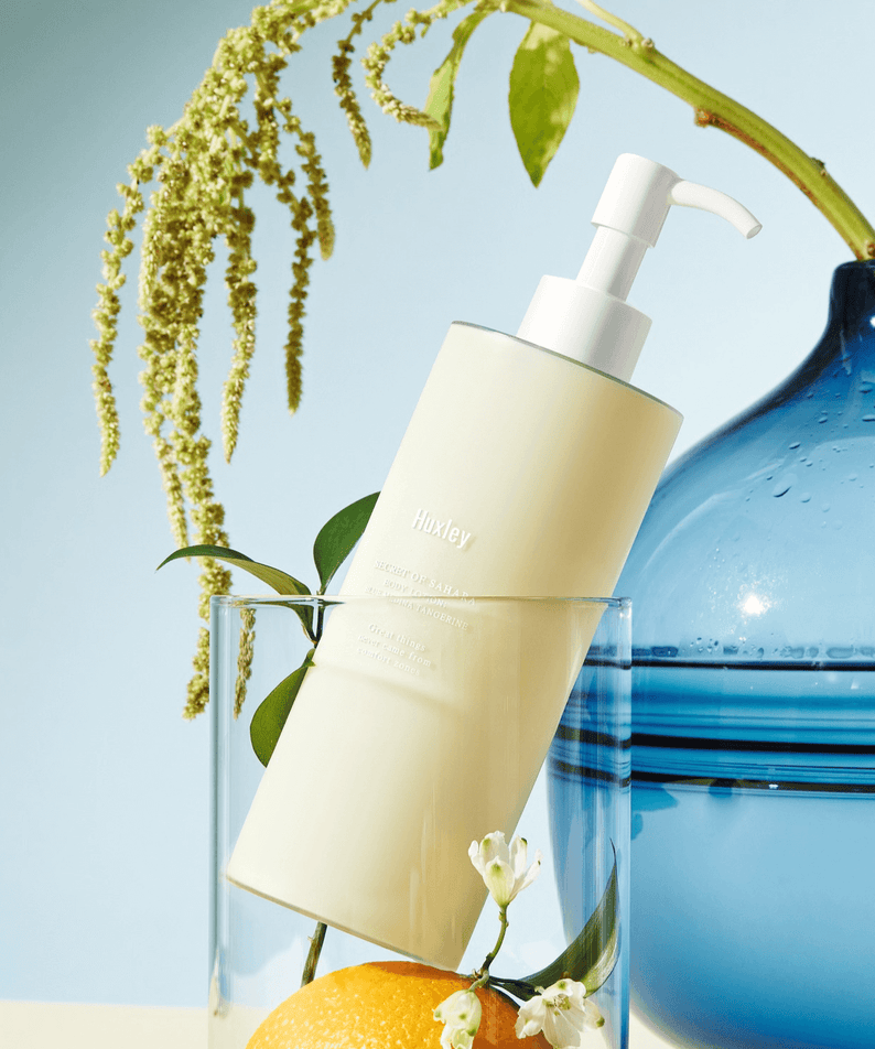HUXLEY Body Lotion Blue Madina Tangerine bottle with pump on display with decorative elements in the background