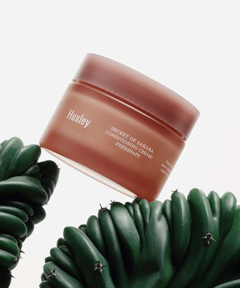 HUXLEY Conditioning Cream Preshape in a brown jar surrounded by green succulents