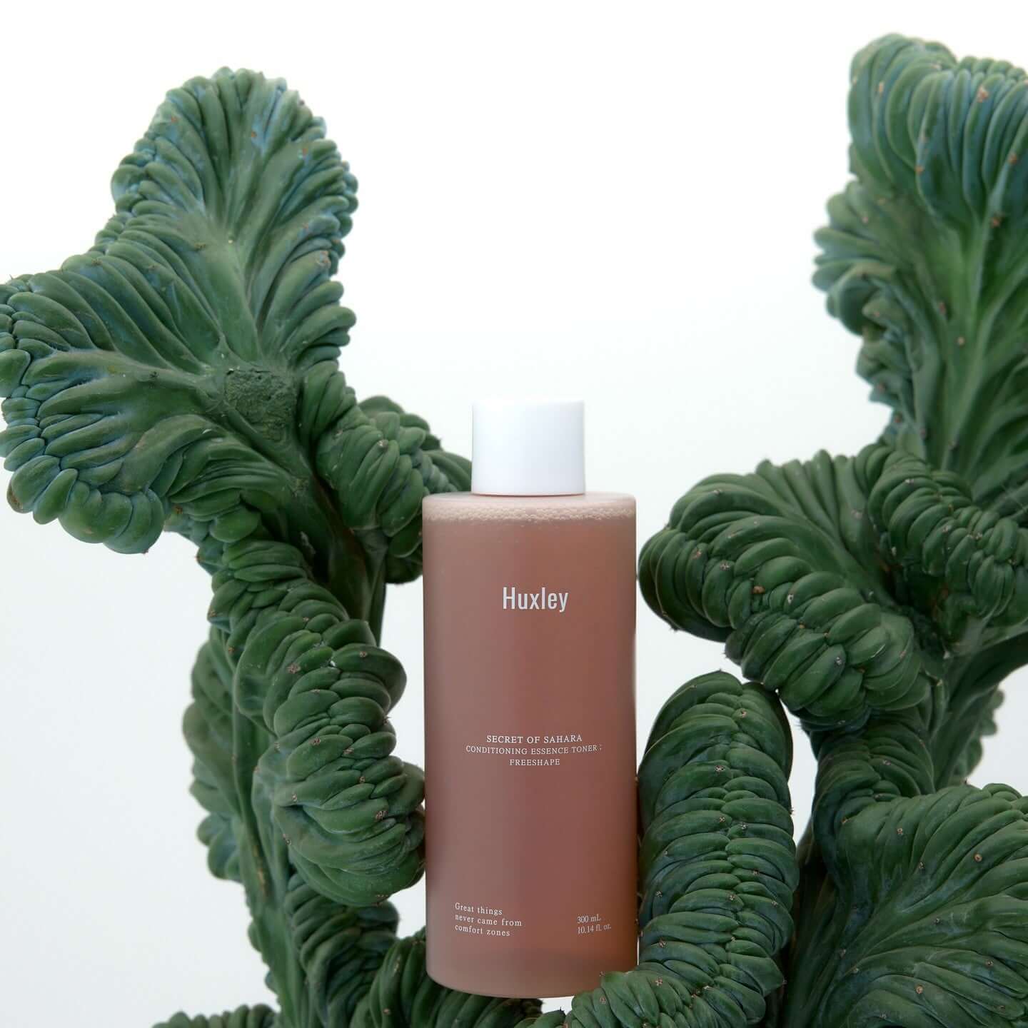 HUXLEY Conditioning Essence Toner Preshape bottle surrounded by green plants, showcasing natural beauty and skincare benefits.