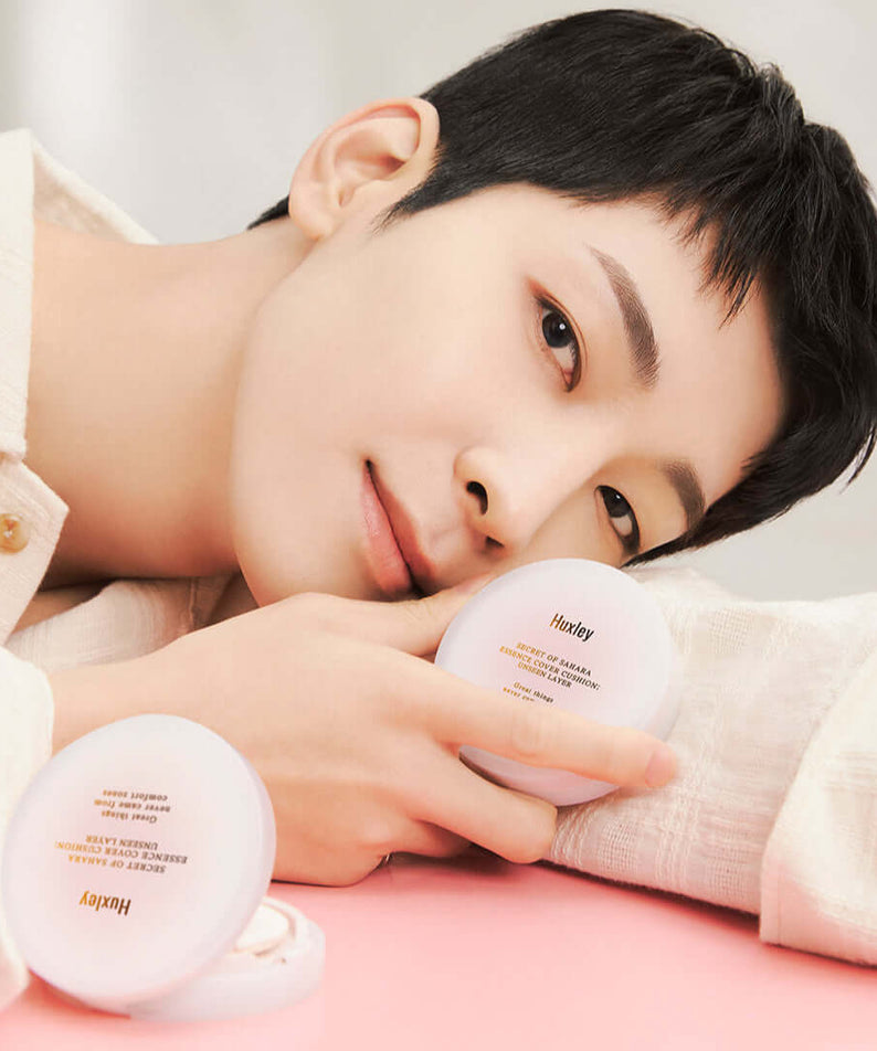 Person holding HUXLEY Essence Cover Cushion Unseen Layer compact with smooth skin and a gentle smile.