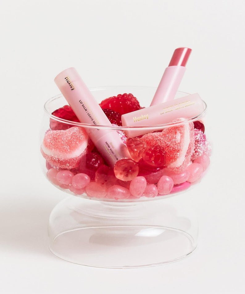 HUXLEY Lip Balm Leave Behide in glass bowl with pink decorative candies