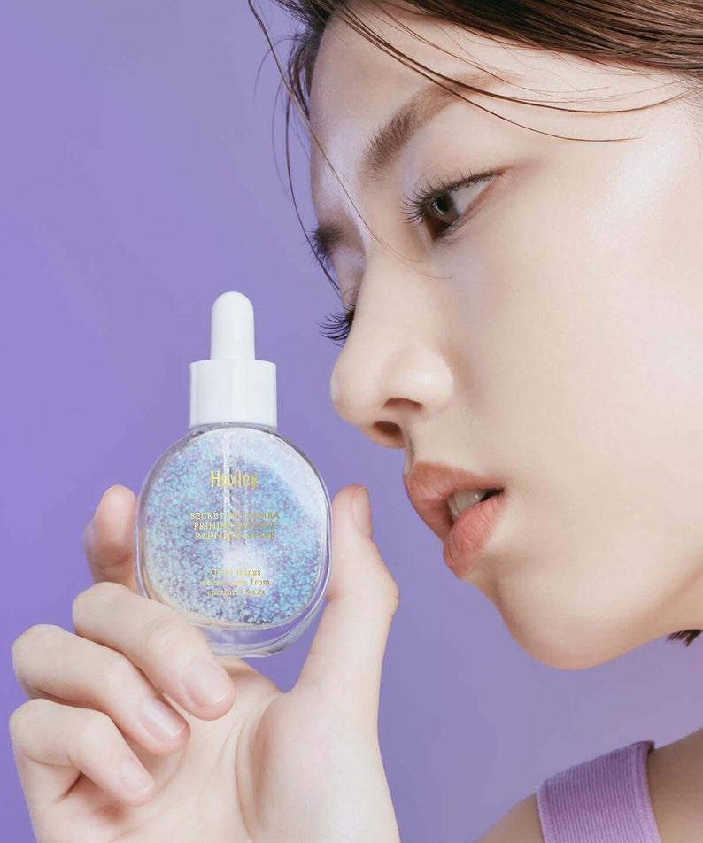 Close-up of woman holding HUXLEY Priming Essence Rediance Layer with glowing skin.