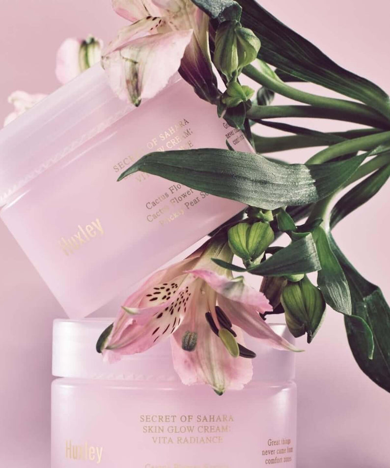 HUXLEY Skin Glow Cream Vita Radiance jars with flowers, promoting enhanced radiance for glowing skin.