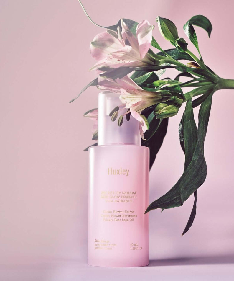 HUXLEY Skin Glow Essence Vita Radiance with floral background, glowing serum bottle promoting radiant skin.