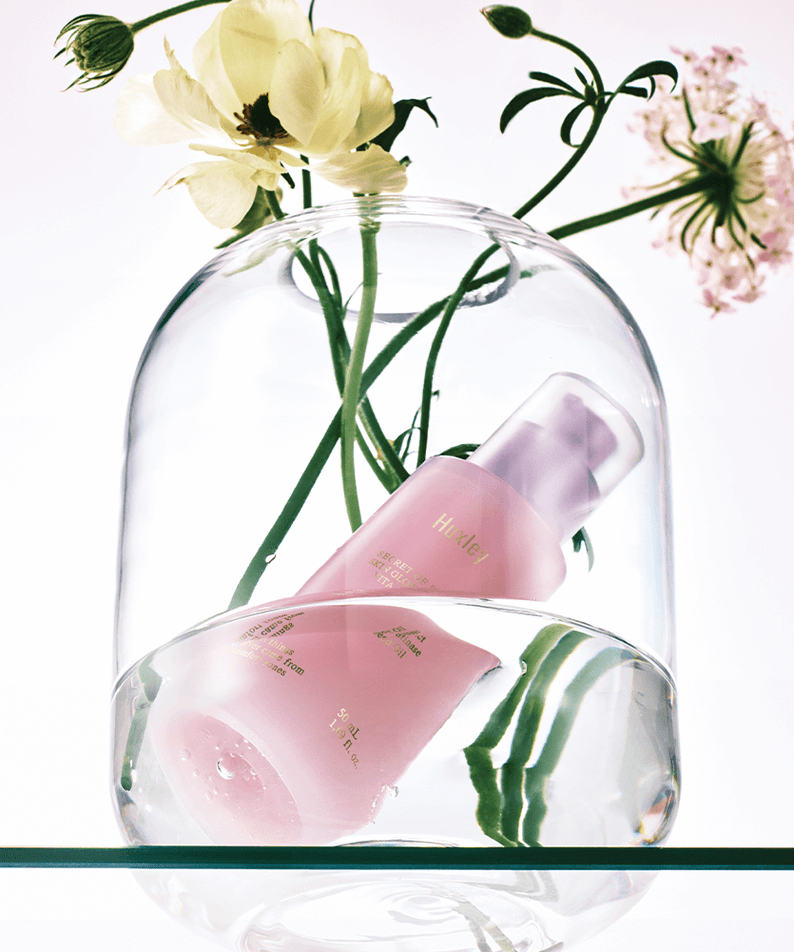 HUXLEY Skin Glow Essence Vita Radiance bottle with flowers under glass dome
