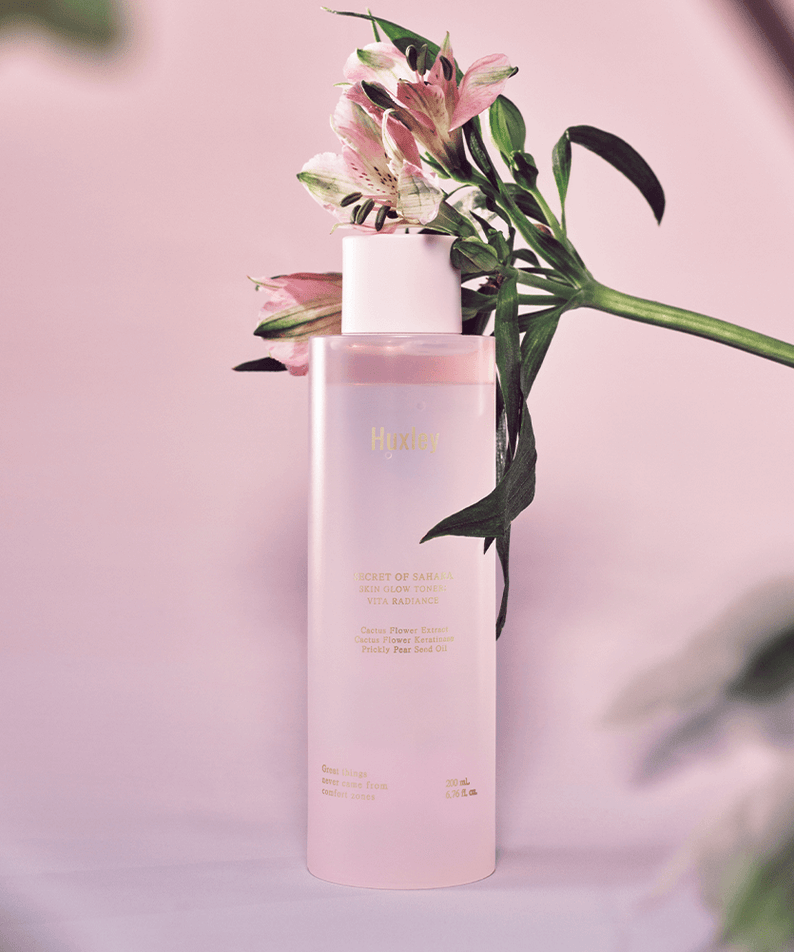 Bottle of HUXLEY Skin Glow Toner Vita Radiance with flowers on a pink background