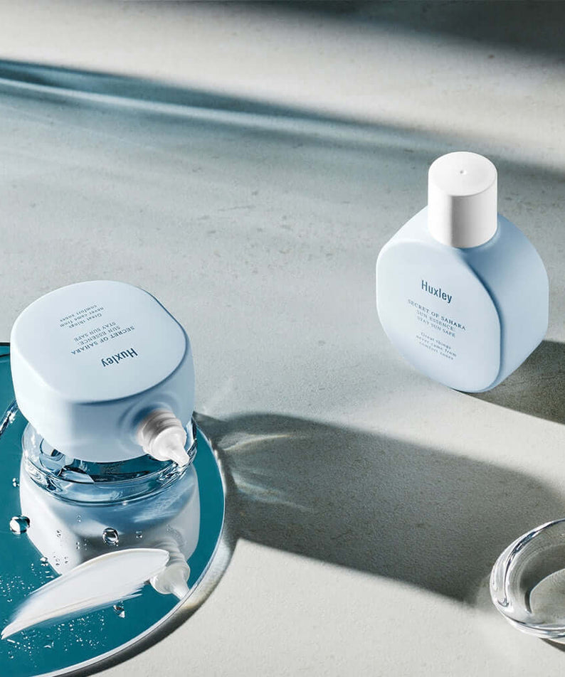 HUXLEY Sun Essence Stay Sun Safe products displayed on a reflective surface with a modern, minimalist design.