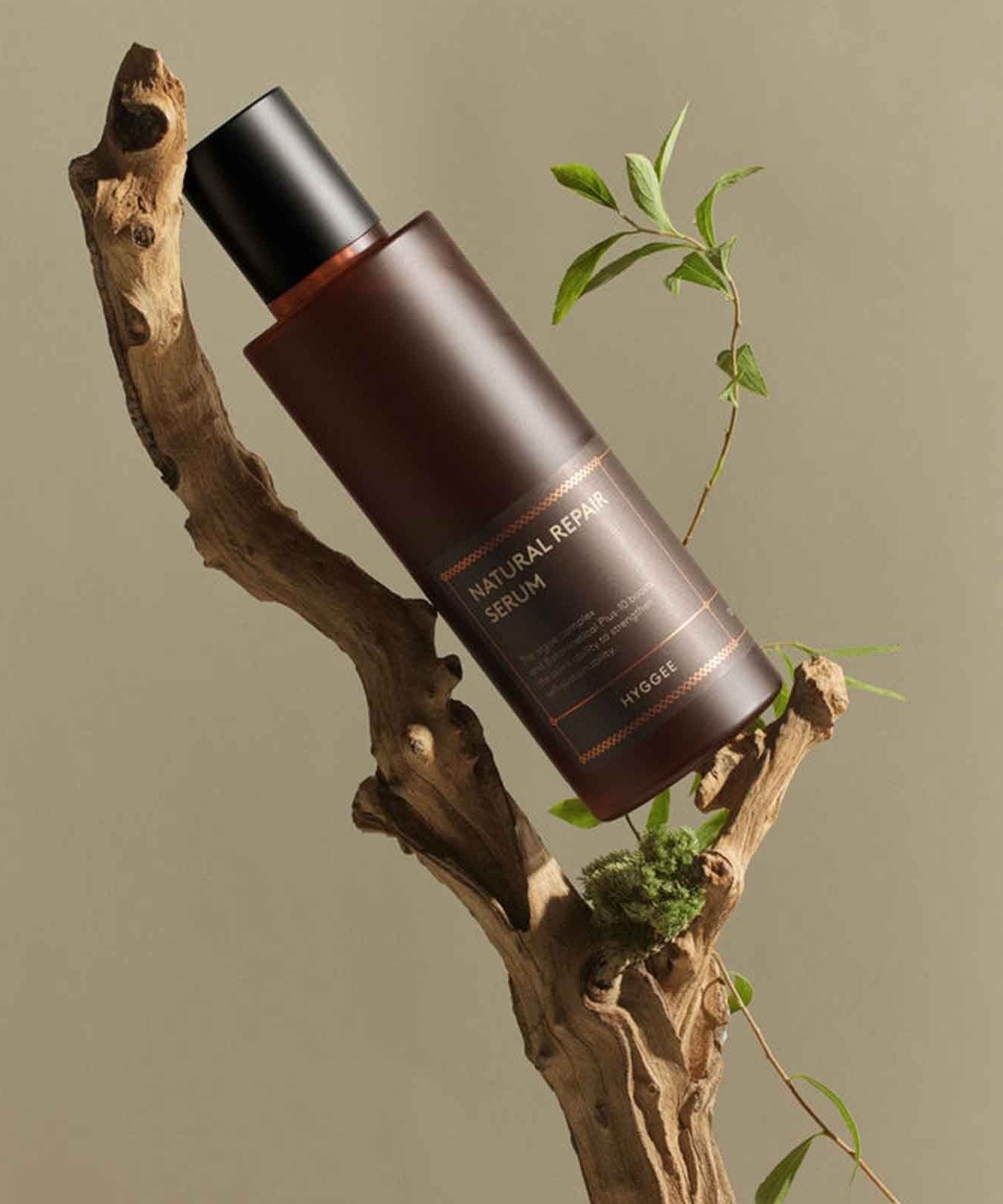 HYGGEE Natural Repair Serum 120ml bottle displayed on a natural wood and plant setting, highlighting organic skincare essence.