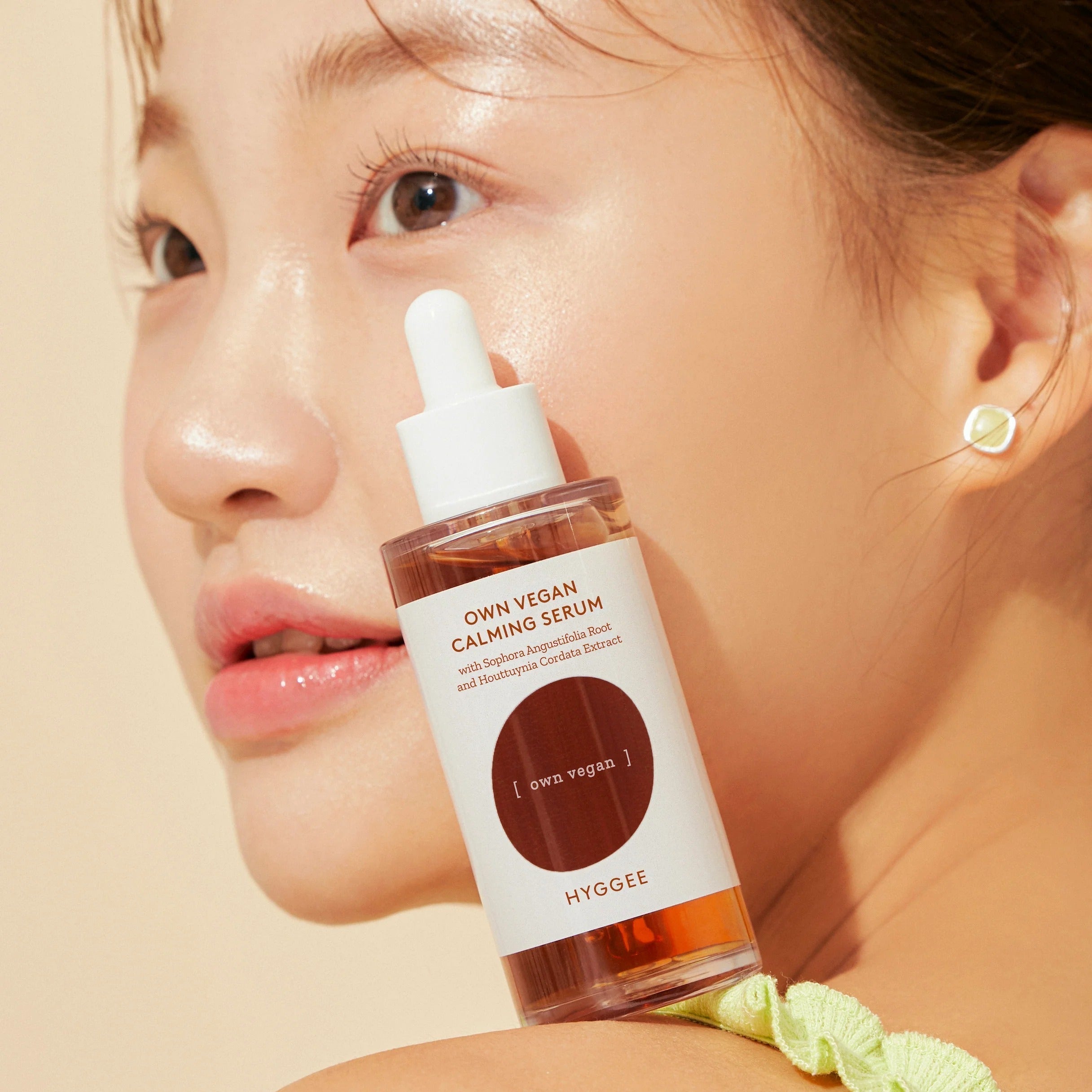 Close-up of a model holding HYGGEE Own Vegan Calming Serum 50ml with glowing skin.