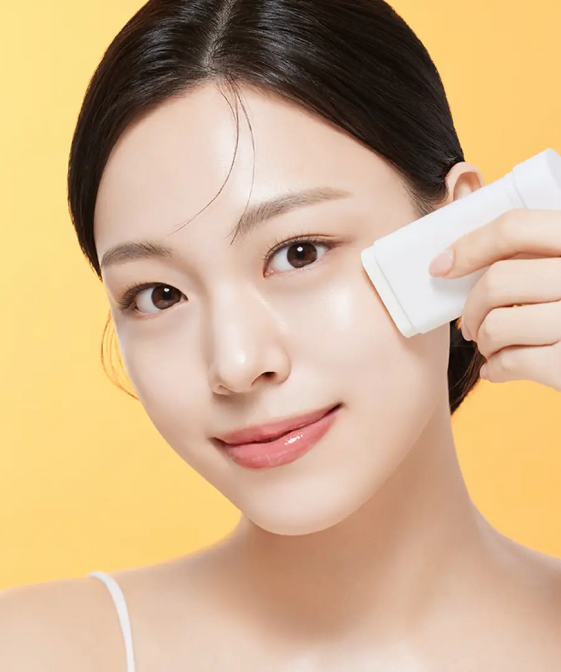 Woman applying ILLIYOON Daily Weaponless Sun Stick 20g on face with yellow background.