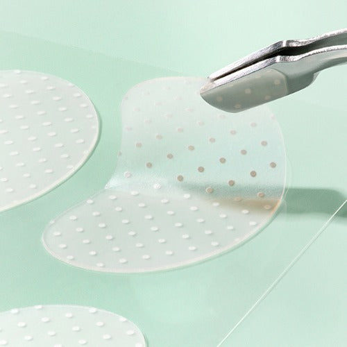 Close-up of ILSO No Trouble Spot Patch being lifted with tweezers, highlighting its texture and transparency.