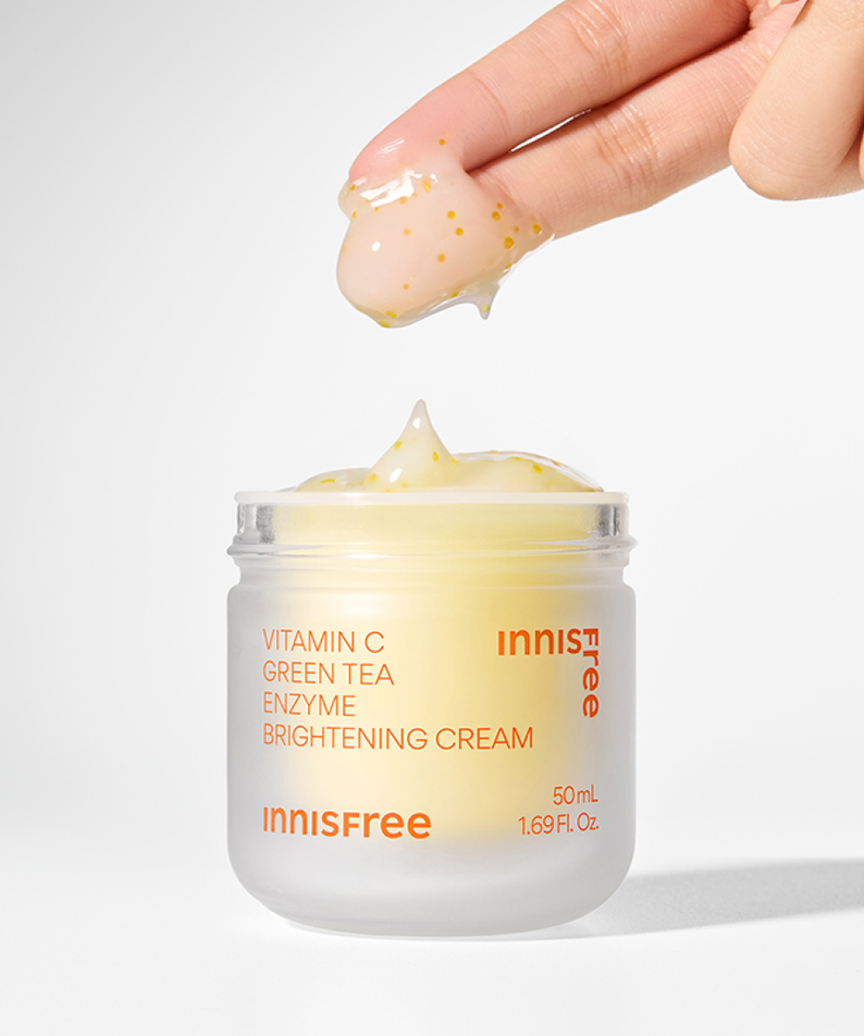 INNISFREE Vitamin C Enzyme Brightening Cream 50ml being applied with fingertips, showcasing texture and packaging.