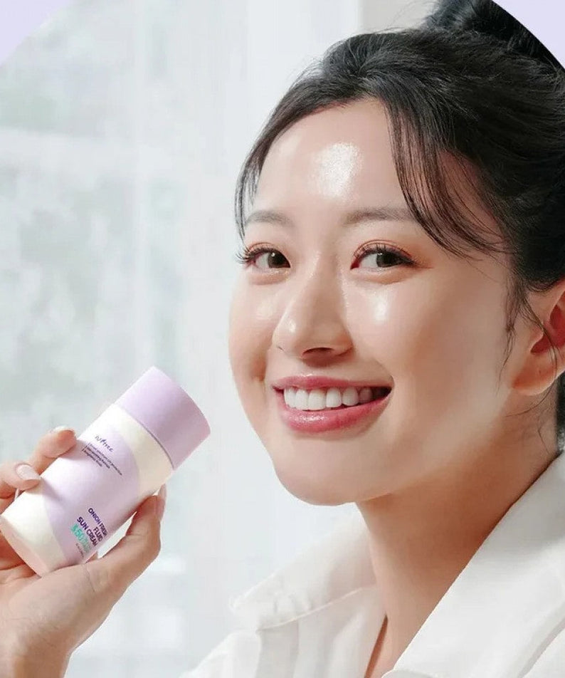 Smiling person holding ISNTREE Onion fresh Fluid Sun Cream 50ml showcasing skincare product.