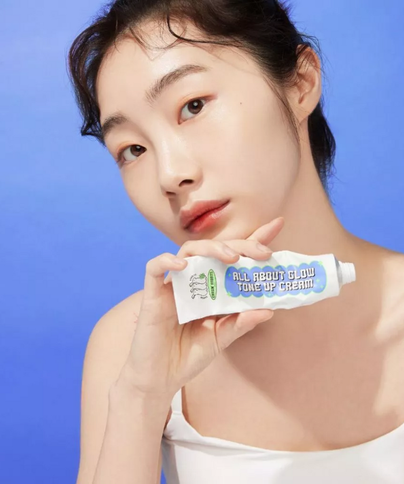 Model holding IT'S SKIN All About Glow Tone Up Cream against a blue background