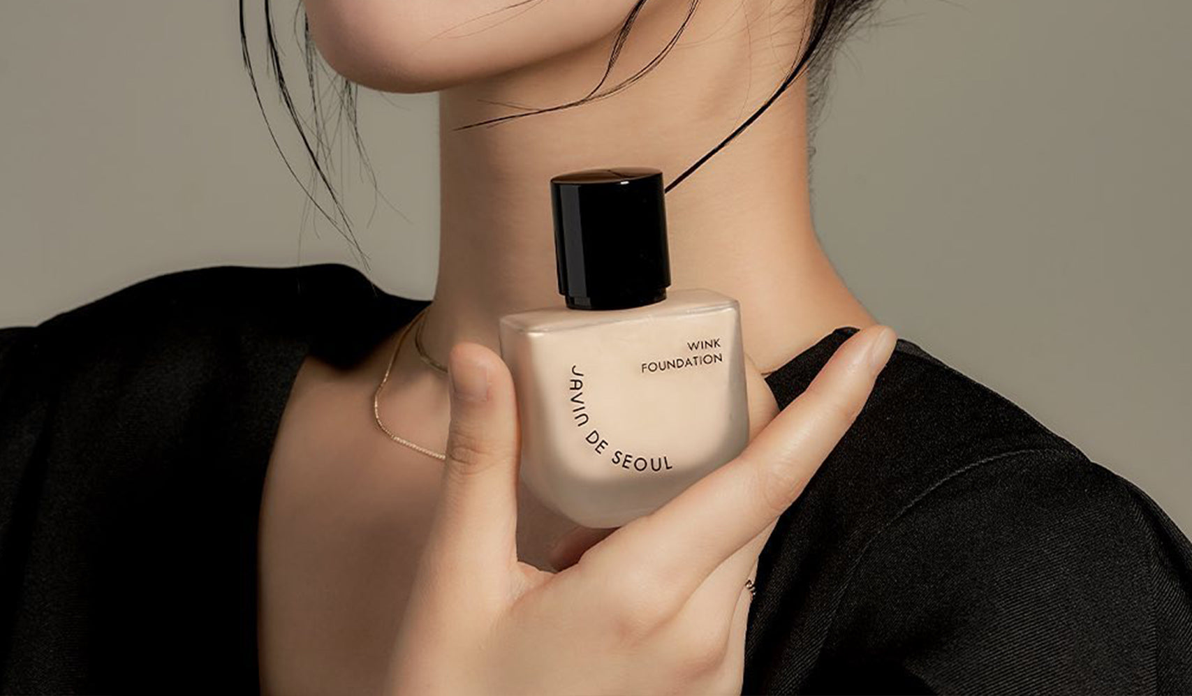 Close-up of a person holding a bottle of Wink Foundation by Seoul with elegant packaging against a neutral background.