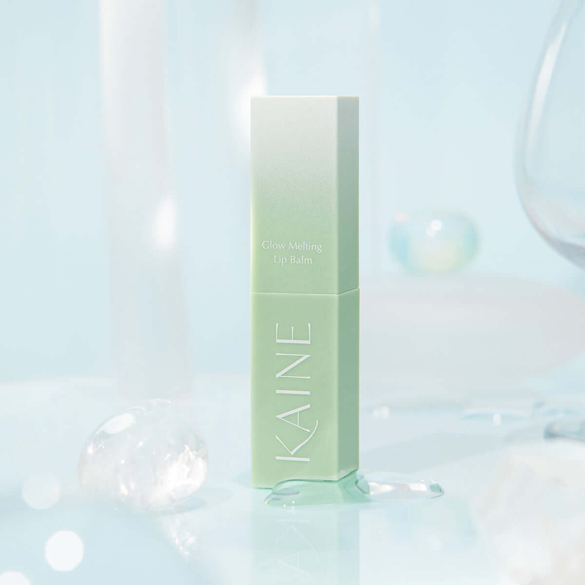 KAINE Glow Melting Lip Balm in pastel green packaging on a light blue background.