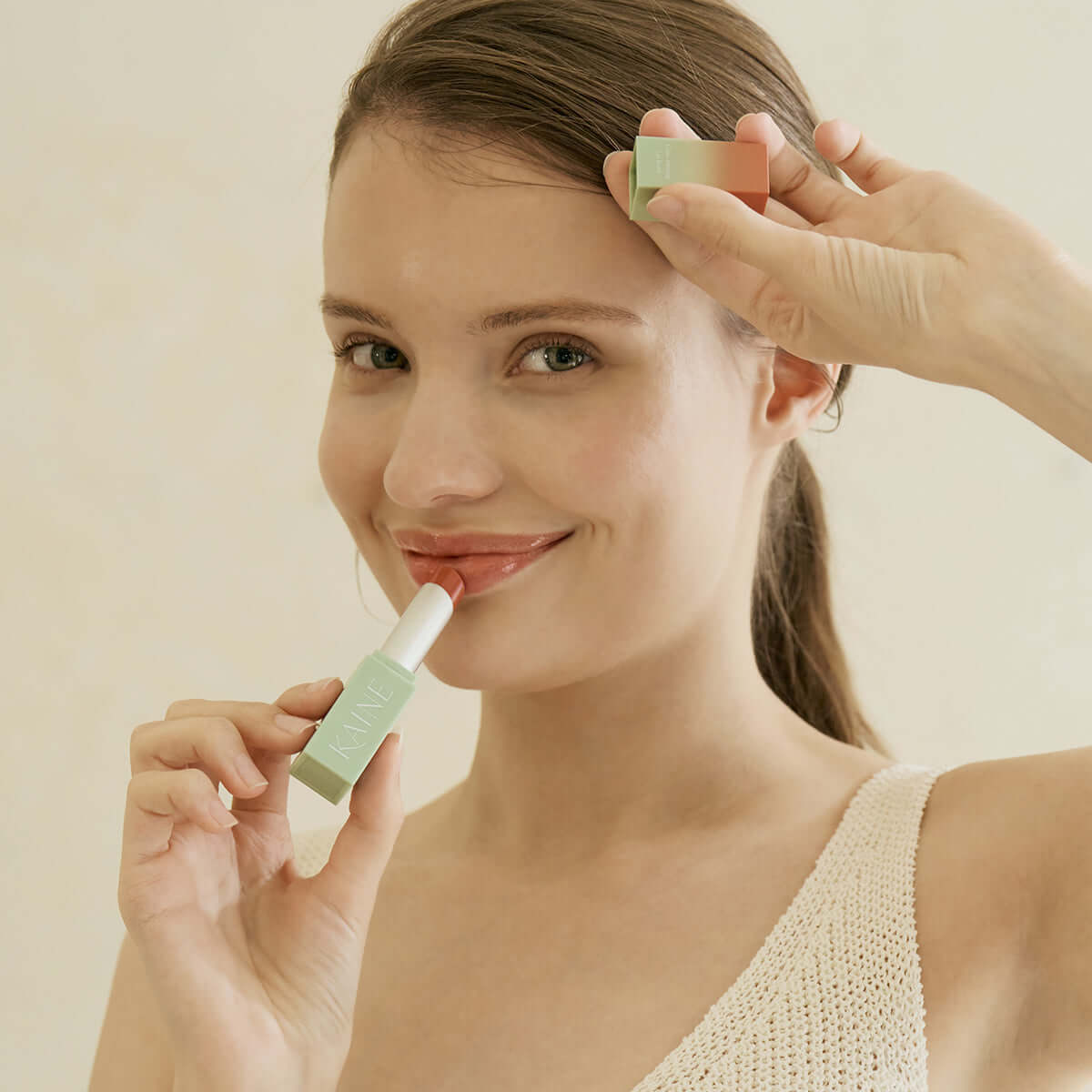 Woman applying KAINE Glow Melting Lip Balm, showcasing the product's packaging and creamy texture for a radiant finish.
