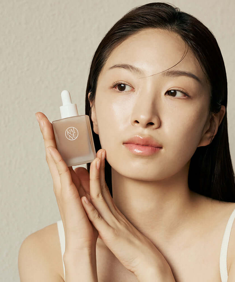 Woman holding KAINE Kombu Barrier Ampoule close to her face, showcasing skincare product and packaging.
