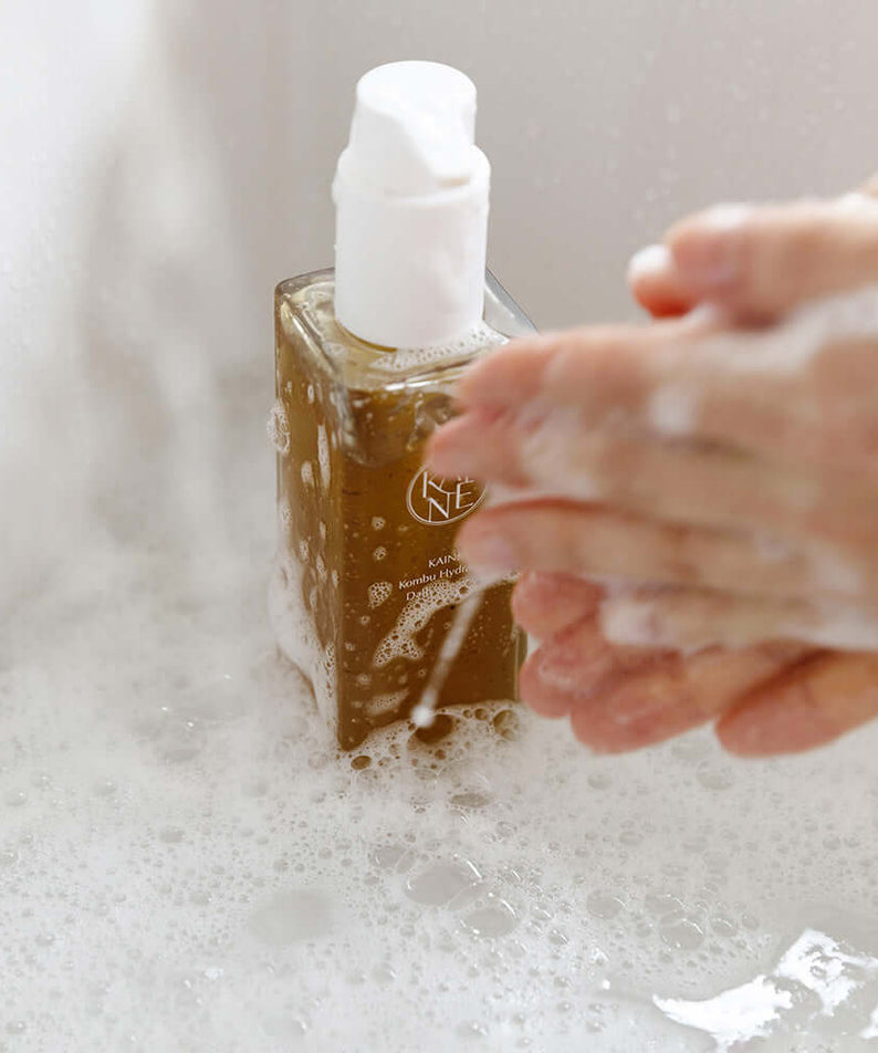 Hands lathering with foam next to KAINE Kombu Hydrating Daily Cleanser 155g bottle