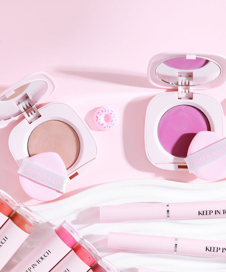 KEEP IN TOUCH GLossy Glow Marine Balm in open containers, showcasing vibrant shades and sleek packaging on a pink background.