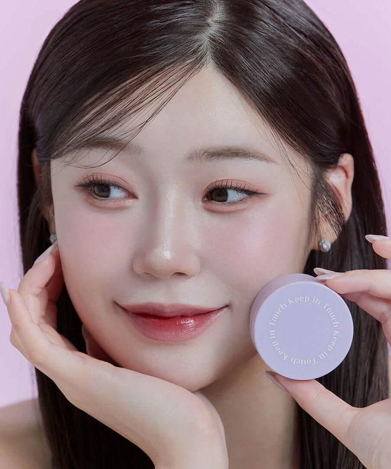 Woman holding KEEP IN TOUCH Mini Pore Eraser Powder with a gentle smile and soft makeup in pastel background.