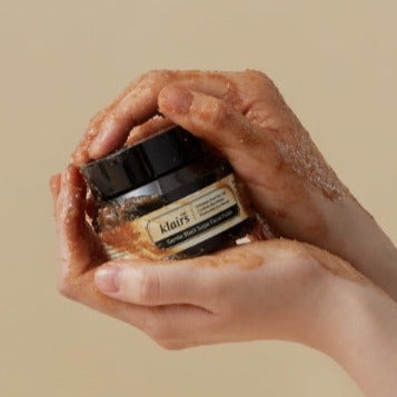 Hands holding jar of KLAIRS Gentle Black Sugar Facial polish 110g with sugar texture visible