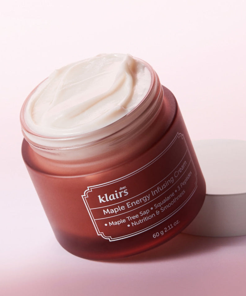 Open jar of KLAIRS Maple Energy Infusing Cream 60g with white cream and labeled brown container on pink background.