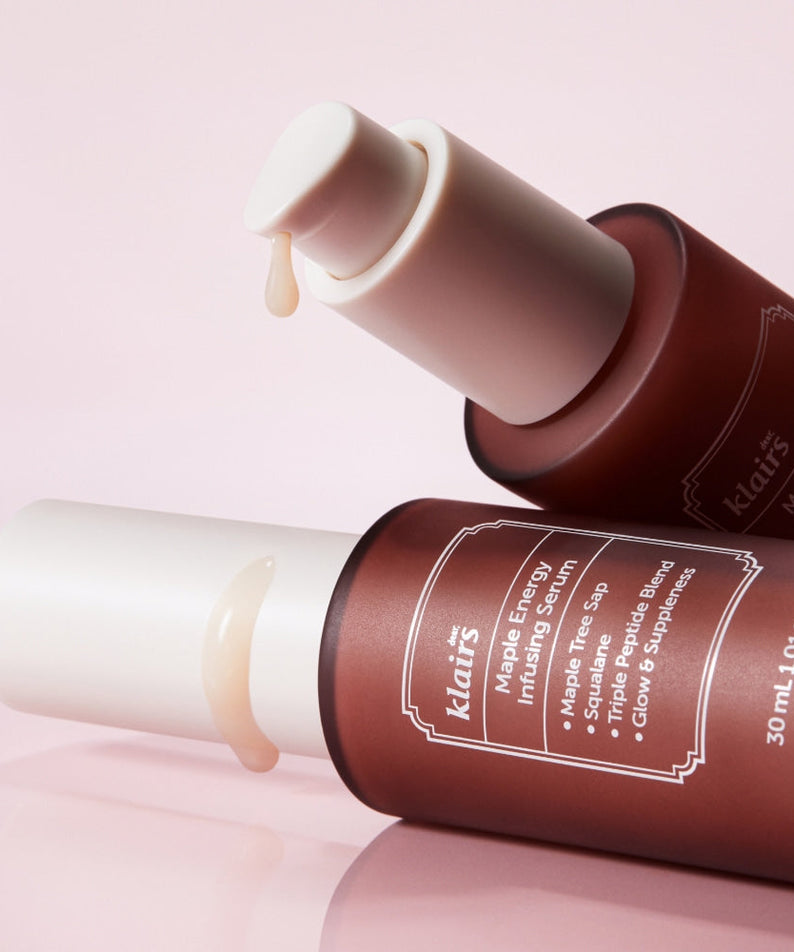 Two bottles of KLAIRS Maple Energy Infusing Serum 30ml with droppers, showcased against a pink background.