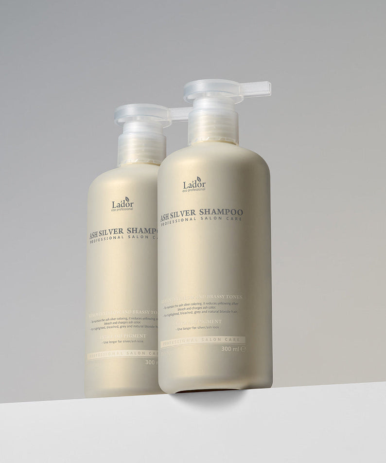 Two bottles of LADOR ASH Silver Shampoo 300ml displayed on a white surface with a neutral background.