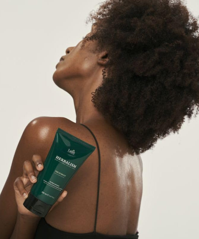 Woman holding LADOR Herbalism Treatment 150ml with visible product label