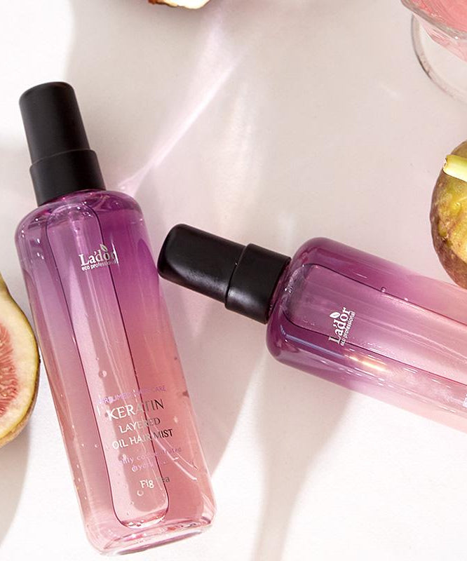 Two bottles of LADOR Keratin Perfume Hair Mist 130ml with figs in the background, showcasing the product's elegant design.