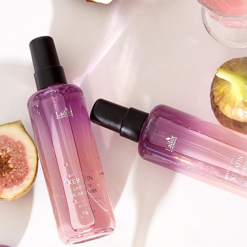 Two bottles of LADOR Keratin Perfume Hair Mist 130ml with figs in the background, showcasing the product's elegant design.