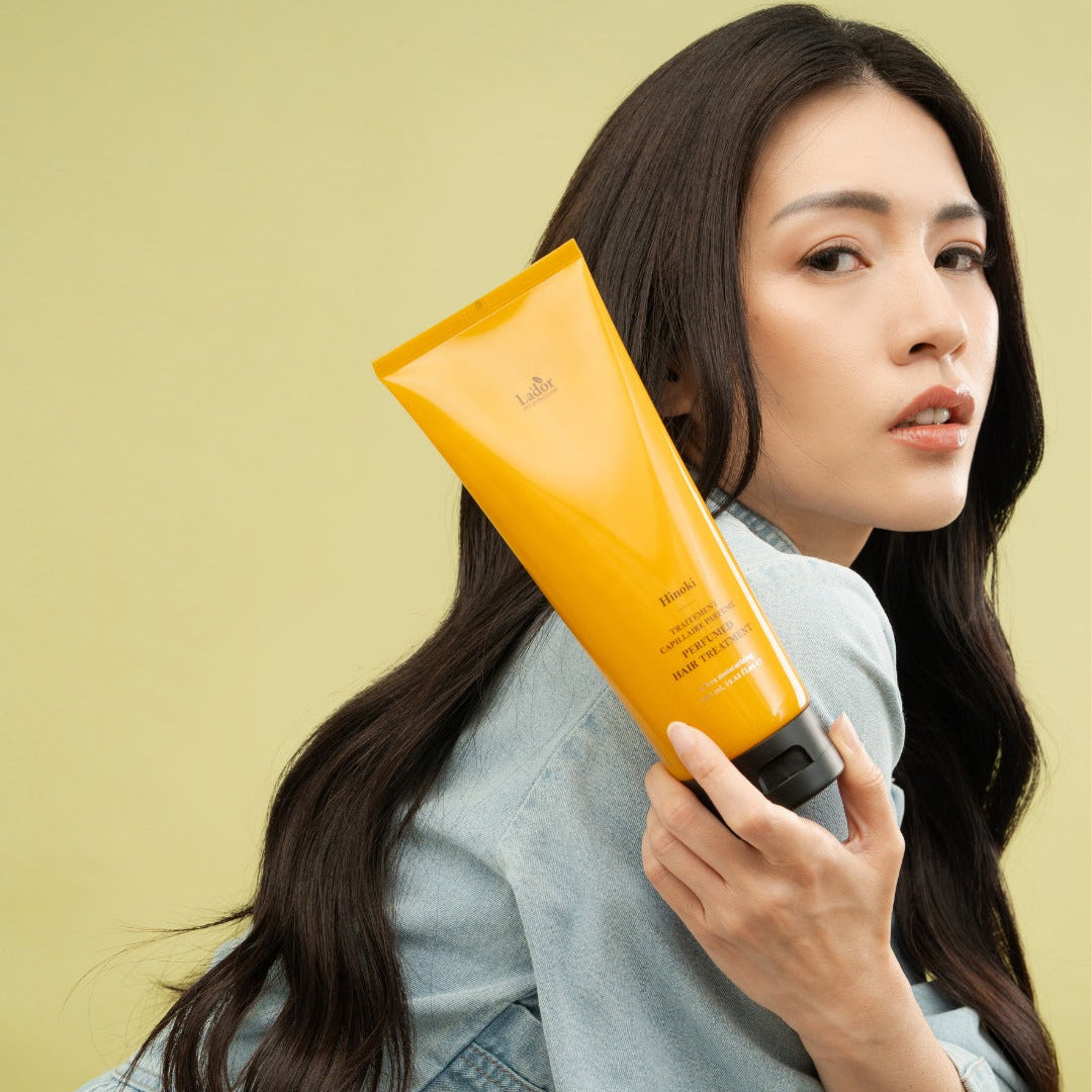 Woman holding LADOR Perfume Hair Treatment 380ml against light green background